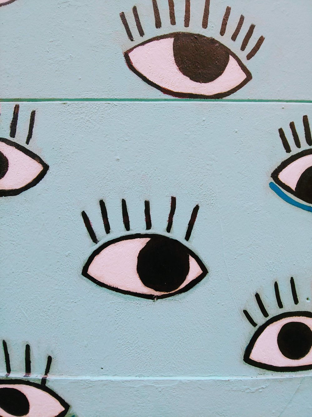 Photo by  erika akire  on  Unsplash . A light blue wall with cartoonish eyes painted on it.