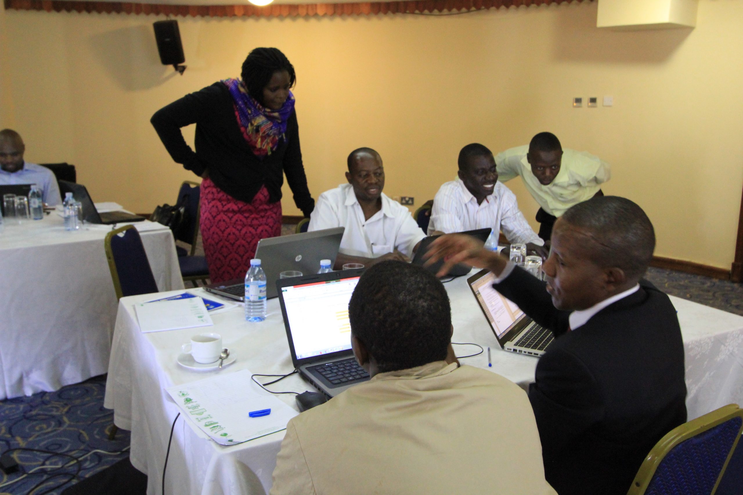 A photo of seven data analysts in Kampala working together on their laptops at a conference room table