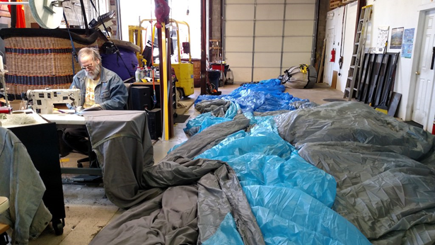 Keith Sproul at a sewing machine with a large balloon, that he is sewing, laid out next to him.