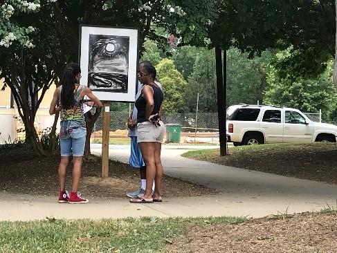 Two women looking at a black and white drawing placed along a trail