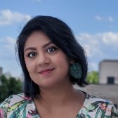 Sadiya smiles and looks at the camera. She is wearing red lipstick, a floral top, and dangly blue earrings. She's probably thinking about how cultural institutions can engage Gen Z! 