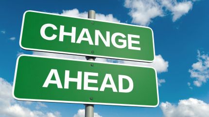 Up close shot of a green and white road sign that reads "CHANGE AHEAD", with a blue sky and clouds visible in the background. 